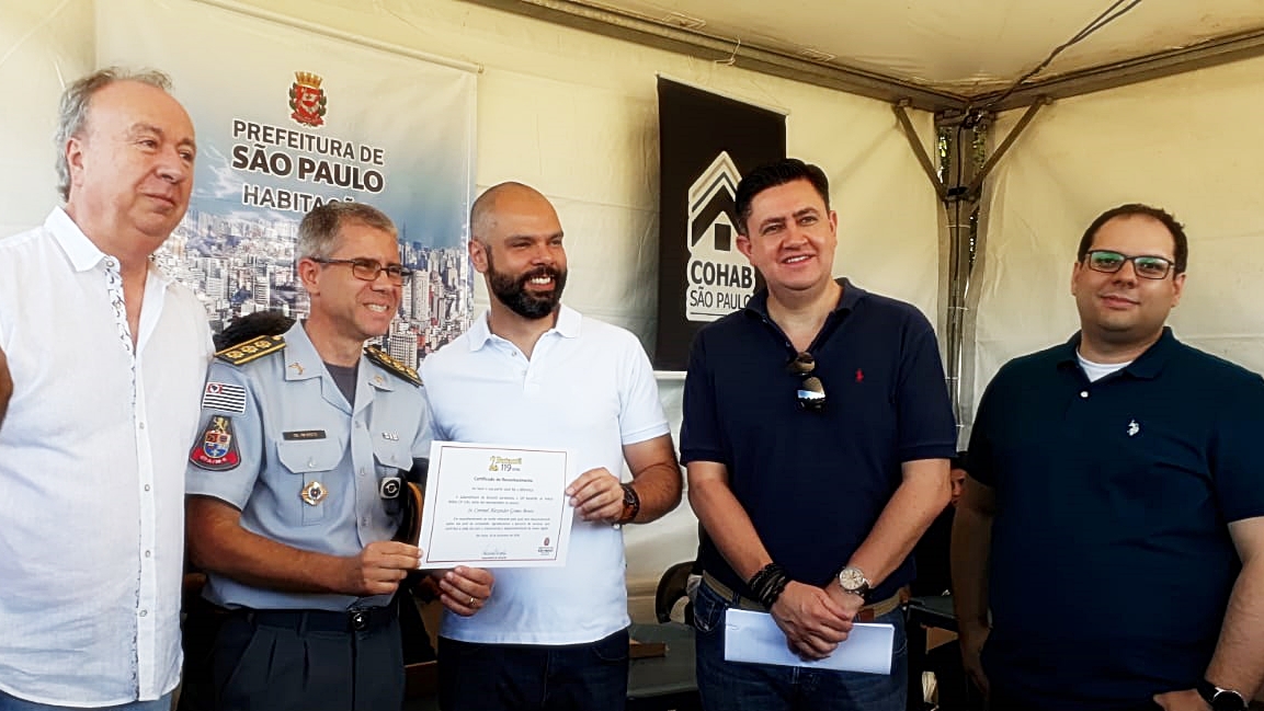 Foto do Prefeito Bruno Covas entregando o certificado de reconhecimento ao Coronel Alexandre Gomes. Estão na foto, além do prefeito e do coronel, o subprefeito e outras duas pessoas.
